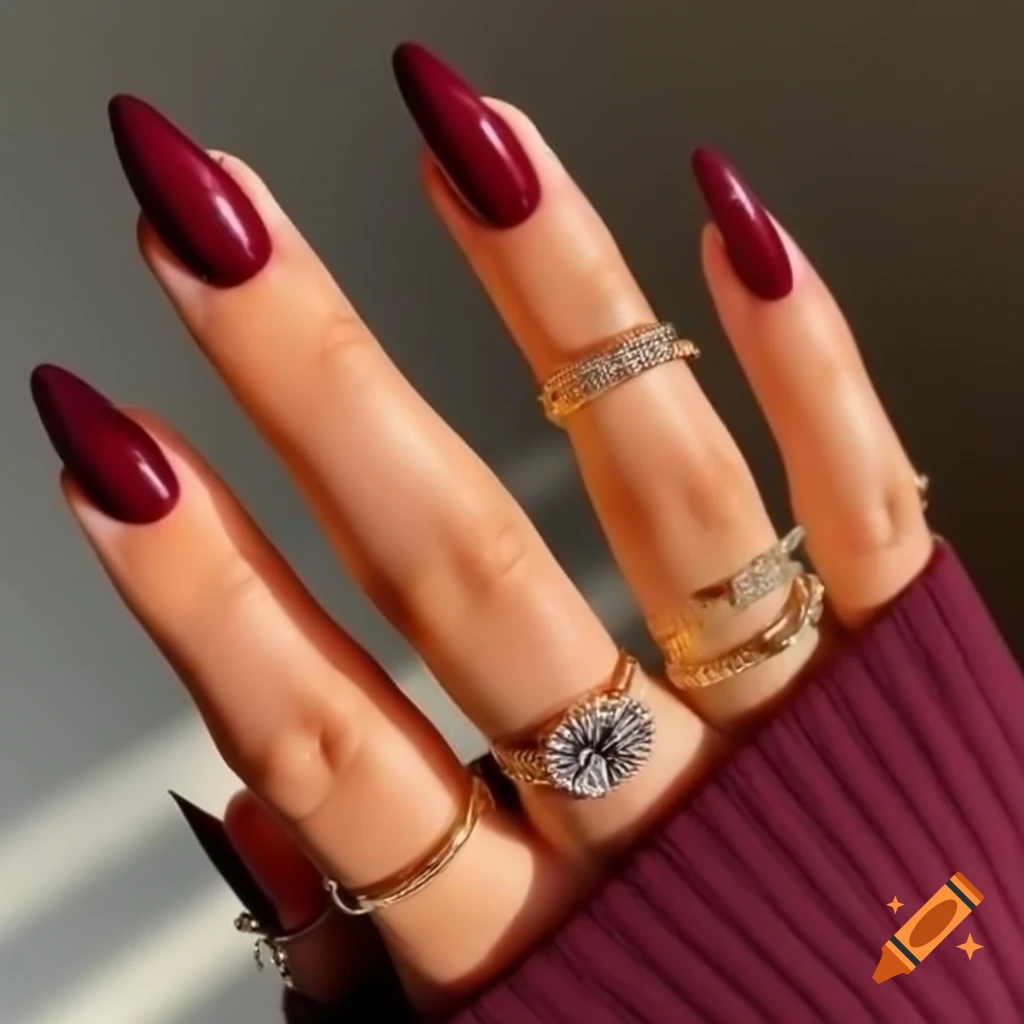 Slender female hand adorned with burgundy ballerina nails and gold diamond rings